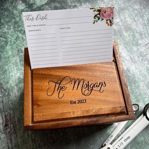 Pu&ograve; includere: Una scatola per ricette in legno con un design floreale sul coperchio. La scatola &egrave; incisa con "The Morgans Est 2023".