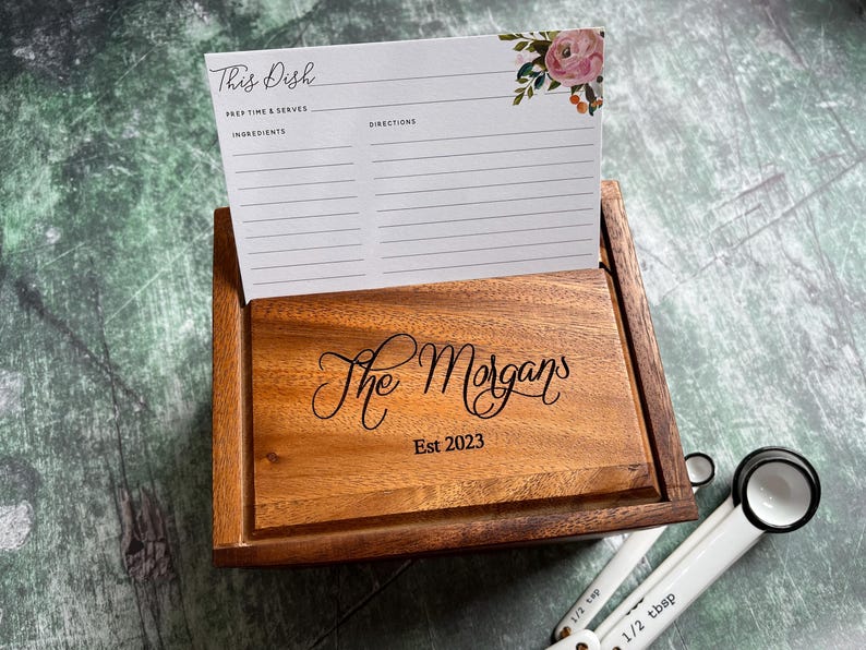 Pu&ograve; includere: Una scatola per ricette in legno con un design floreale sul coperchio. La scatola &egrave; incisa con "The Morgans Est 2023".