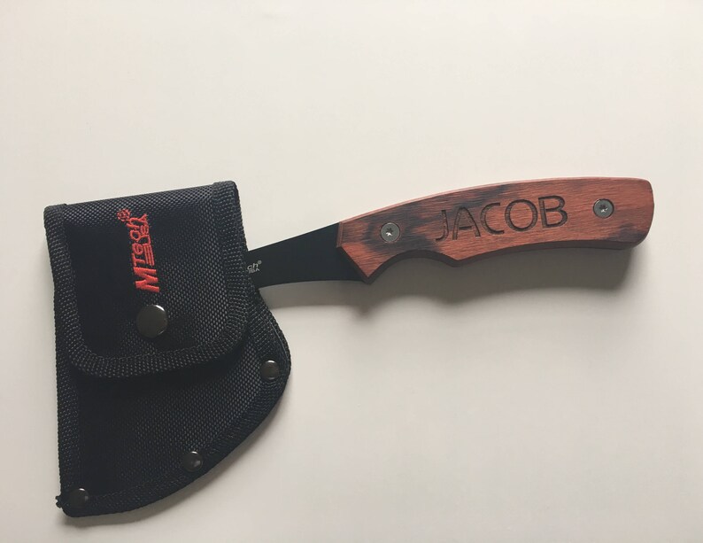 May include: A small black and brown axe with a wooden handle. The handle is engraved with the name "JACOB". The axe comes with a black nylon sheath.