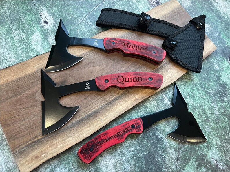 May include: Three black hatchet-style throwing knives with red wooden handles. The handles are engraved with the names "Molitor", "Quinn", and "Sroensman".