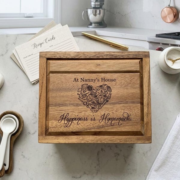 Könnte beinhalten: Eine rechteckige Rezeptbox aus Holz mit Klappdeckel, die den eingravierten Text At Nanny's House, eine herzförmige Collage aus Küchenutensilien und den Schriftzug Happiness is Homemade auf der Vorderseite aufweist.