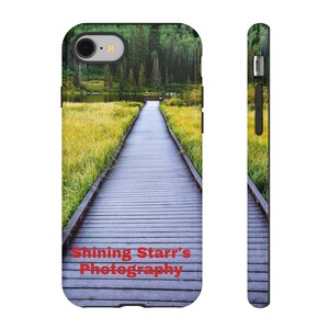 Puede incluir: Una funda para teléfono con una foto de una pasarela de madera que conduce a través de un campo de hierba hacia un lago y un bosque en el fondo. El texto "Shining Starr's Photography" está impreso en la parte inferior de la funda.