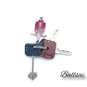 May include: A red and silver scooter keychain with two leather key covers, one blue and one brown. The keychain has a silver ring and two keys.
