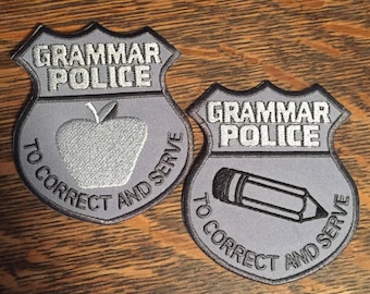 Könnte beinhalten: Zwei graue Grammar Police-Aufnäher mit schwarzem Rand. Ein Aufnäher zeigt einen grauen Apfel, der andere einen grauen Bleistift. Beide Aufnäher tragen die Worte "Grammar Police" und "To Correct and Serve" in silbernen Buchstaben.