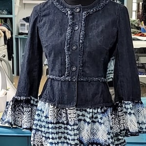 May include: A dark blue denim jacket with a ruffled trim and a white and blue patterned skirt underneath.