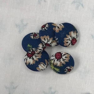 Peut inclure: Assortiment de boutons en tissu bleu avec des motifs floraux blancs et rouges. Les boutons sont disposés en deux groupes sur un fond blanc.