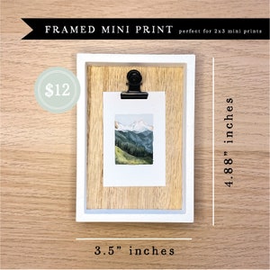 May include: A framed mini print of a watercolor painting of a mountain landscape. The frame is made of wood and has a white border. The print is 2 inches by 3 inches and the frame is 3.5 inches by 4.88 inches.