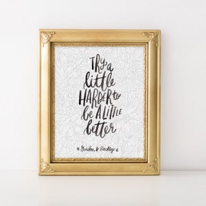 May include: A framed print with a white background and a black floral pattern. The print features a quote in black script that reads "Try a little harder to be a little better." The quote is attributed to Gordon B. Hinckley.