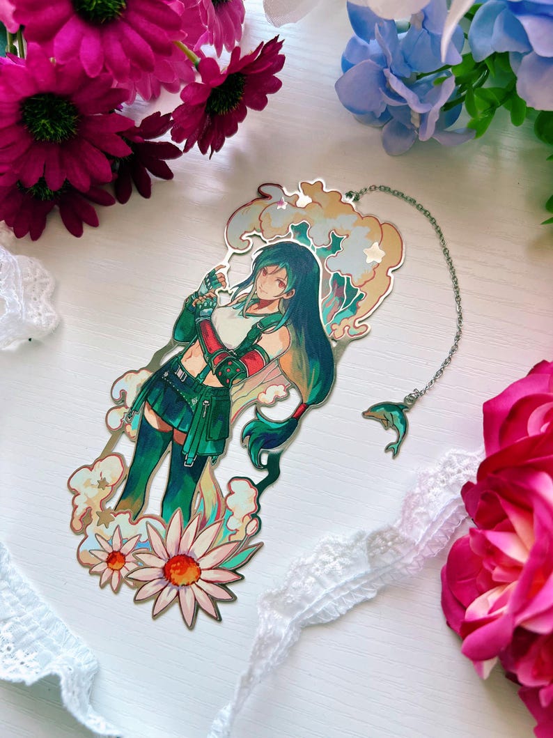 May include: A metal bookmark featuring a long-haired character in a green outfit, surrounded by stylized clouds and flowers. The bookmark has a silver chain attached with a small dolphin charm. The design includes soft pastel colors and intricate outlines.