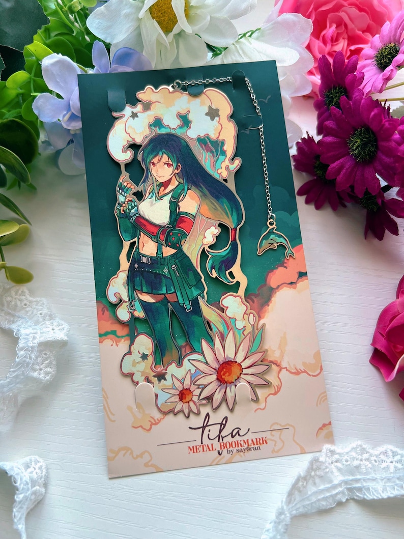 May include: A metal bookmark featuring an anime-style character with long dark hair, wearing a white top and green skirt, surrounded by stylized clouds and flowers. A thin silver chain with a small dolphin charm is attached to the top of the bookmark.