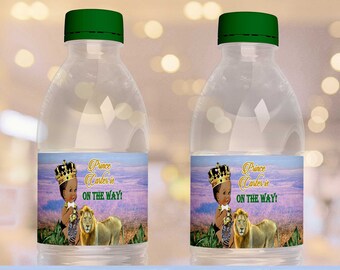 May include: Printable water bottle labels featuring a cartoon baby boy wearing a crown and a lion. The labels have a jungle theme with a purple and green background. The text on the labels reads "Prince Carter is on the way!"