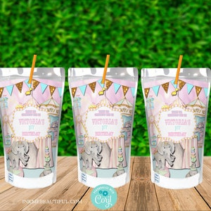 K&ouml;nnte beinhalten: Zwei durchsichtige Plastikbeutel mit einem rosafarbenen und blauen Zirkus-Design. Die Beutel haben Strohhalme und sind mit "Victoria's 1st Birthday" beschriftet.