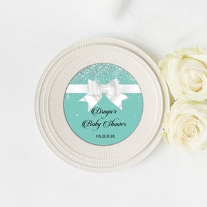 Puede incluir: Un c&iacute;rculo azul turquesa y plata con purpurina con un lazo blanco y el texto "Draya's Baby Shower 04.21.2024".