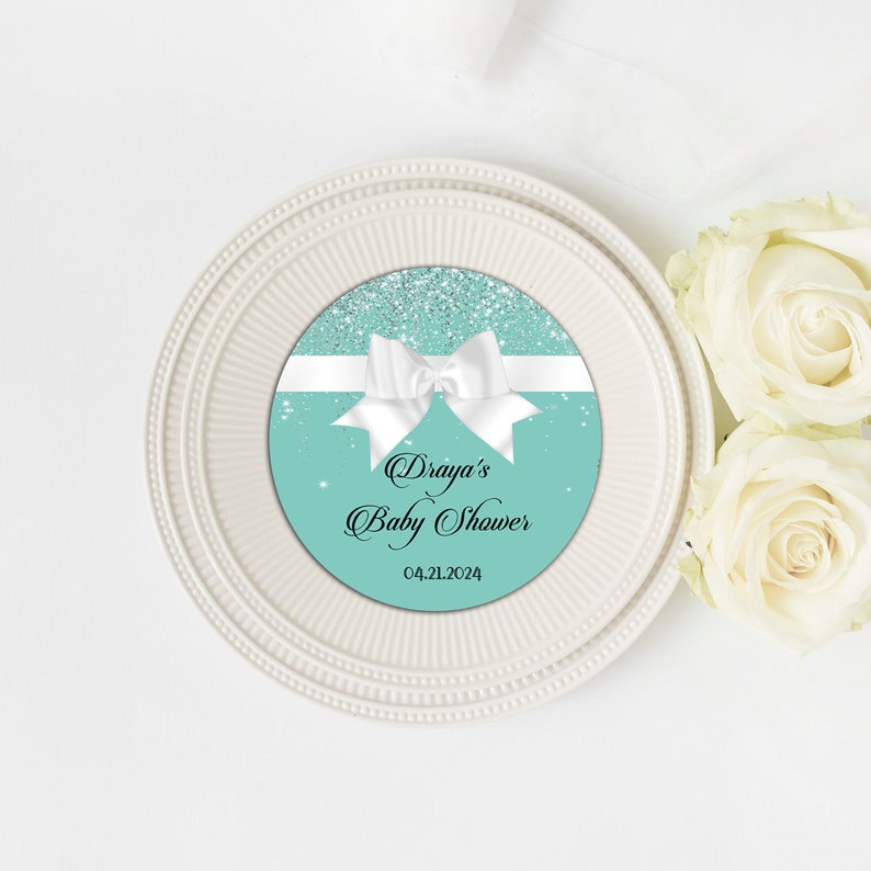 Puede incluir: Un c&iacute;rculo azul turquesa y plata con purpurina con un lazo blanco y el texto "Draya's Baby Shower 04.21.2024".