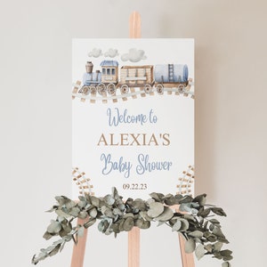 May include: A white welcome sign with a blue and brown train illustration. The sign reads "Welcome to Alexia's Baby Shower 09.22.23".