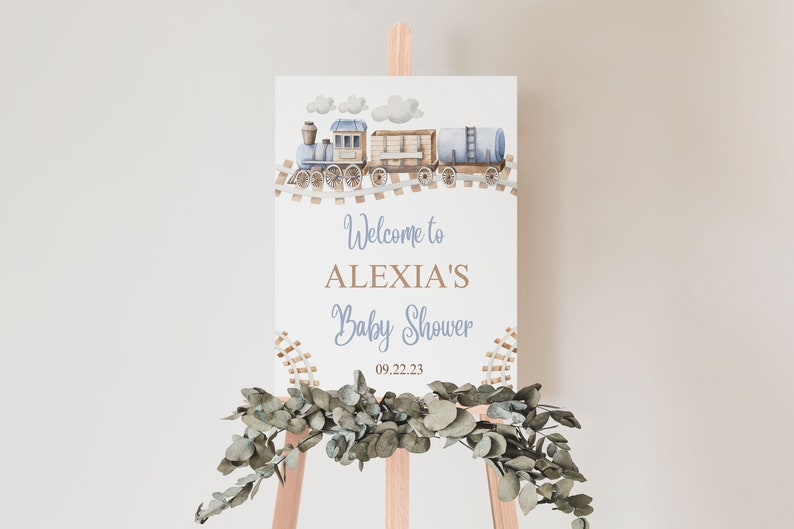 May include: A white welcome sign with a blue and brown train illustration. The sign reads "Welcome to Alexia's Baby Shower 09.22.23".