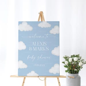 May include: A blue and white baby shower welcome sign with clouds and the text "Welcome to Alexis & Mark's Baby Shower 09.16.2024".