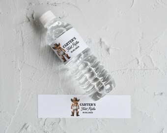 May include: A white water bottle label with a cartoon cowboy wearing a diaper and boots. The label says "Carter's First Rodeo 10.02.2024".