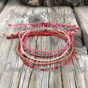 May include: A stack of minimalist adjustable bracelets and anklets in shades of red, pink, and orange. The image includes the text "Minimalist Adjustable Bracelet/Anklet" and "Choose from over 80 colors!" on a wooden surface.