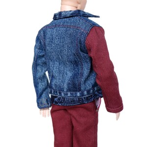 May include: A doll wearing a blue denim jacket with maroon sleeves, maroon shorts, and a brown bun hairstyle.