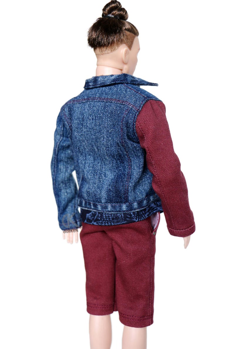 May include: A doll wearing a blue denim jacket with maroon sleeves, maroon shorts, and a brown bun hairstyle.