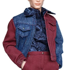 May include: A doll wearing a denim jacket with one red sleeve and one blue sleeve. The doll is also wearing a blue patterned shirt and red pants.
