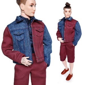 May include: A doll wearing a denim and burgundy jacket with matching burgundy shorts. The doll has short brown hair and brown eyes.