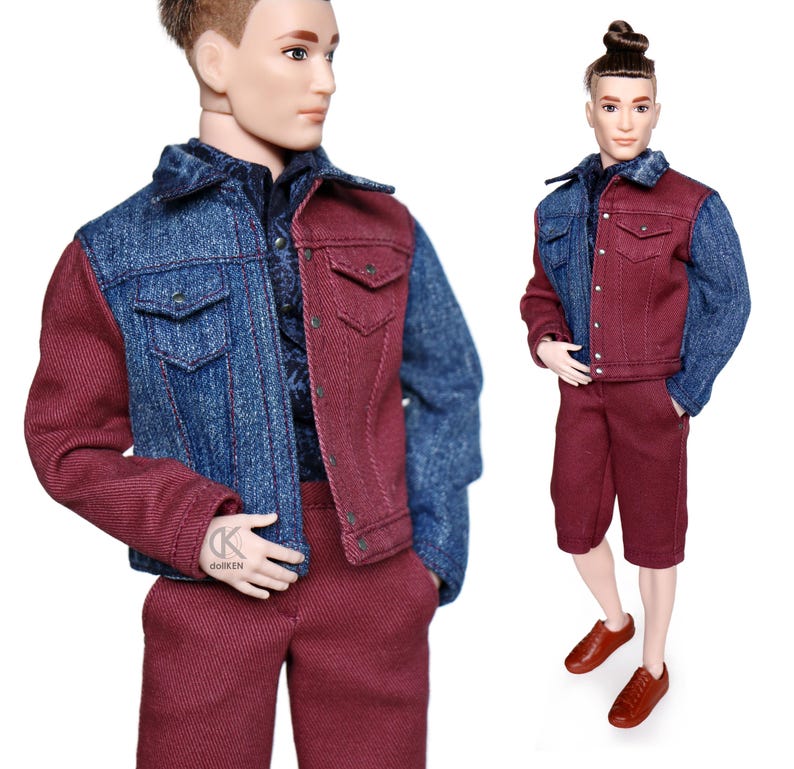 May include: A doll wearing a denim and burgundy jacket with matching burgundy shorts. The doll has short brown hair and brown eyes.