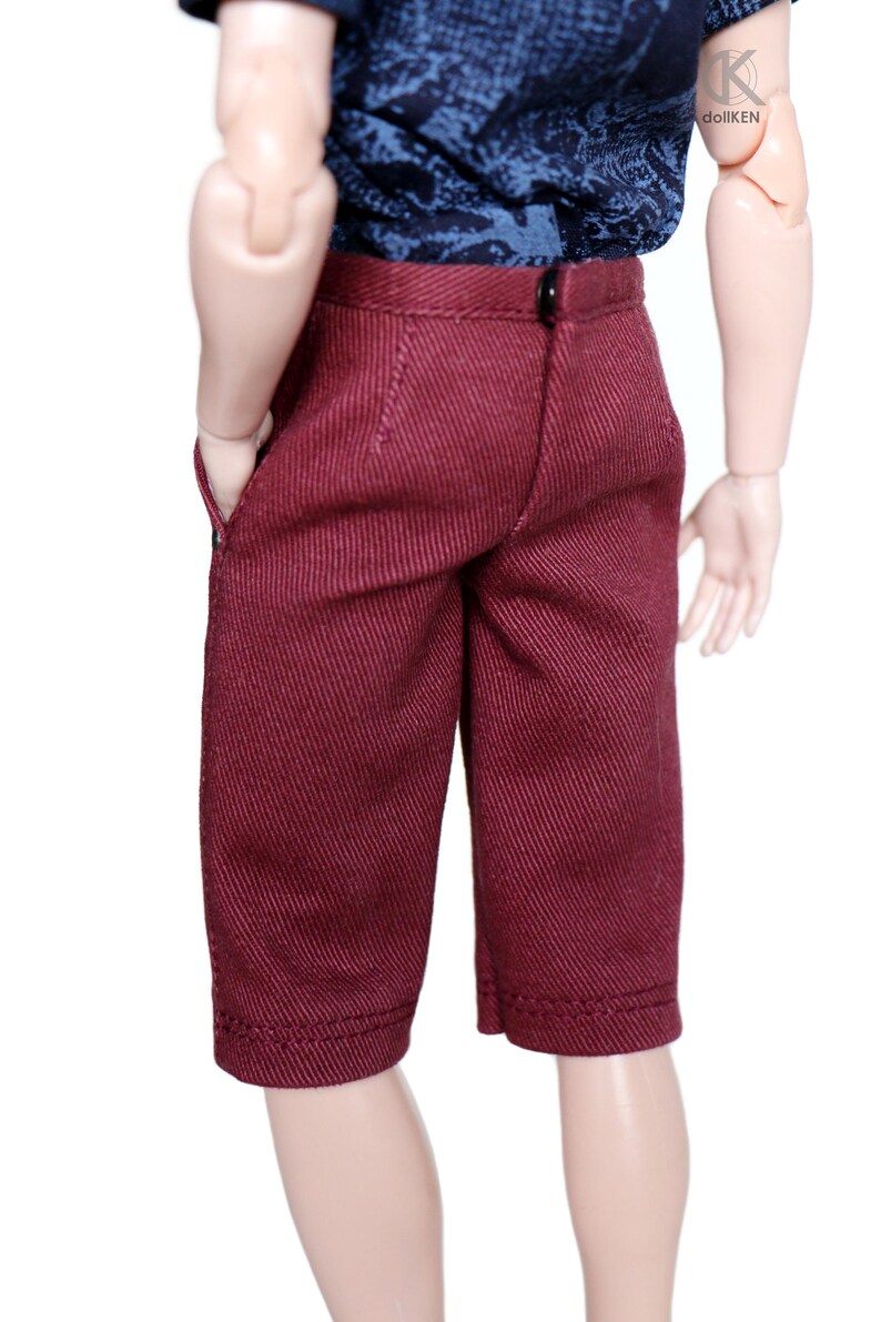 May include: A pair of maroon shorts with a textured fabric. The shorts have a button and zipper closure and two pockets.