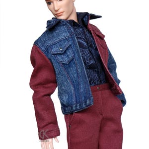 May include: A doll wearing a denim jacket with one red sleeve and red pants. The doll has brown hair in a bun and a shaved side.