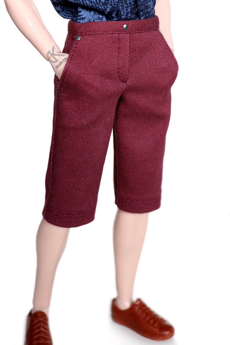 May include: A pair of maroon shorts with a button fly and a single button closure at the waist. The shorts have a straight leg and are made of a textured fabric.