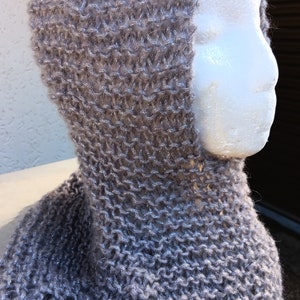 May include: A gray knitted cowl neck with a hood. The cowl is made of a soft, fuzzy yarn with a subtle shimmer.