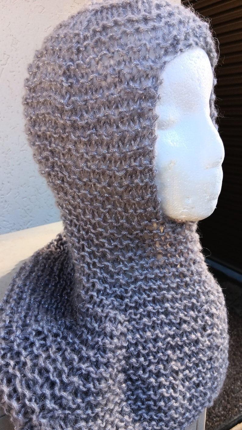 May include: A gray knitted cowl neck with a hood. The cowl is made of a soft, fuzzy yarn with a subtle shimmer.