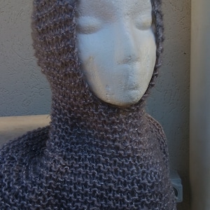 May include: A gray knitted cowl neck scarf with a hood. The scarf is made of a soft, fuzzy yarn.