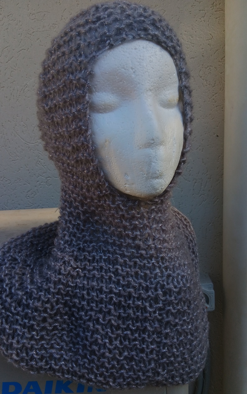May include: A gray knitted cowl neck scarf with a hood. The scarf is made of a soft, fuzzy yarn.
