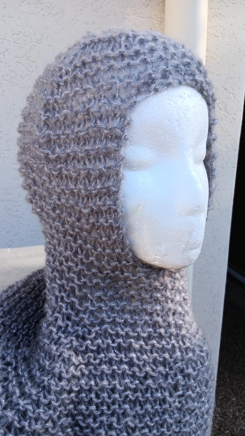 May include: A gray knitted cowl with a hood. The cowl is made of a soft, fuzzy yarn and has a loose, drapey fit.
