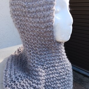 May include: A gray knitted cowl with a hood. The cowl is made with a fuzzy yarn that has a subtle sparkle.