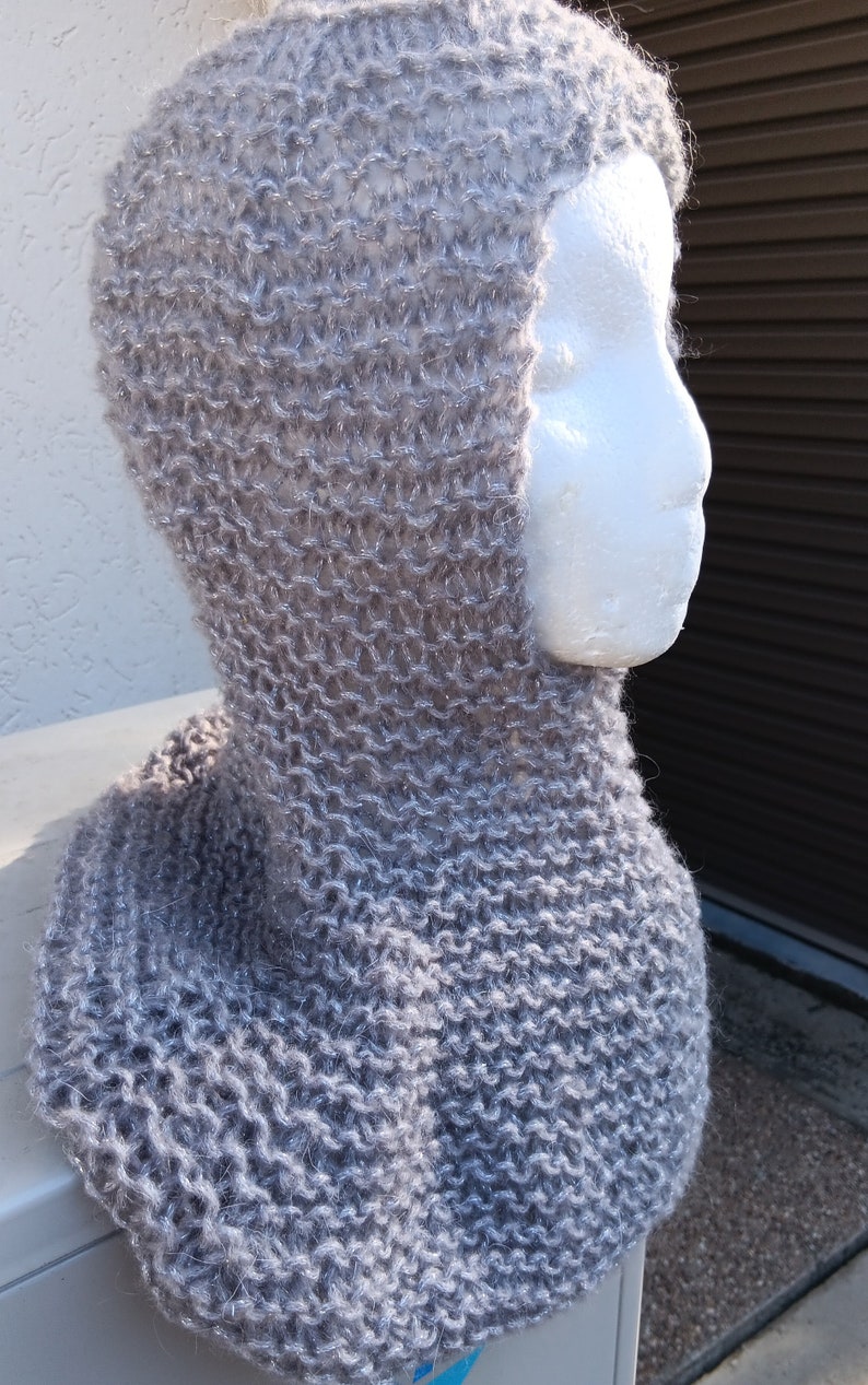 May include: A gray knitted cowl with a hood. The cowl is made with a fuzzy yarn that has a subtle sparkle.