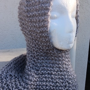 May include: A gray knitted hooded cowl with a soft, fuzzy texture. The cowl is made with a simple stitch pattern and has a long, flowing shape.