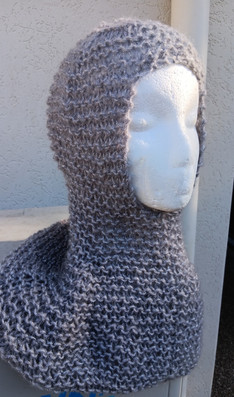 May include: A gray knitted hooded cowl with a soft, fuzzy texture. The cowl is made with a simple stitch pattern and has a long, flowing shape.