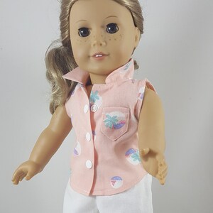 Peut inclure: Une poup&eacute;e portant une chemise rose sans manches avec un imprim&eacute; palmier et un short blanc. La poup&eacute;e a les cheveux blonds et les yeux bruns. La poup&eacute;e porte des sandales blanches avec une boucle.