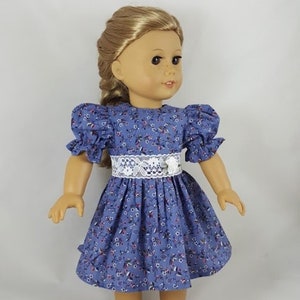 May include: A doll wearing a blue and white floral dress with a white lace belt and white sandals.