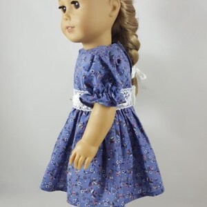 May include: A doll wearing a blue and white floral dress with a white lace trim and white sandals.