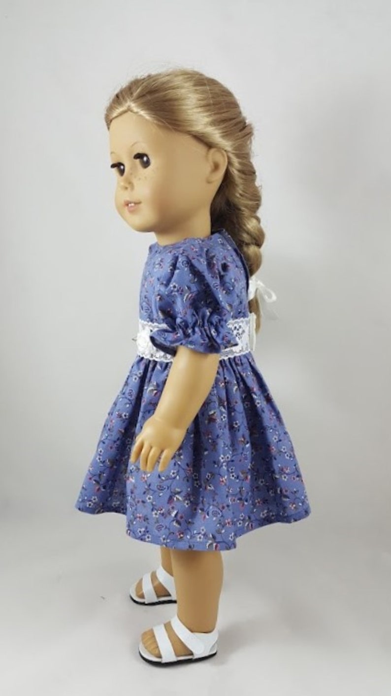May include: A doll wearing a blue and white floral dress with a white lace trim and white sandals.