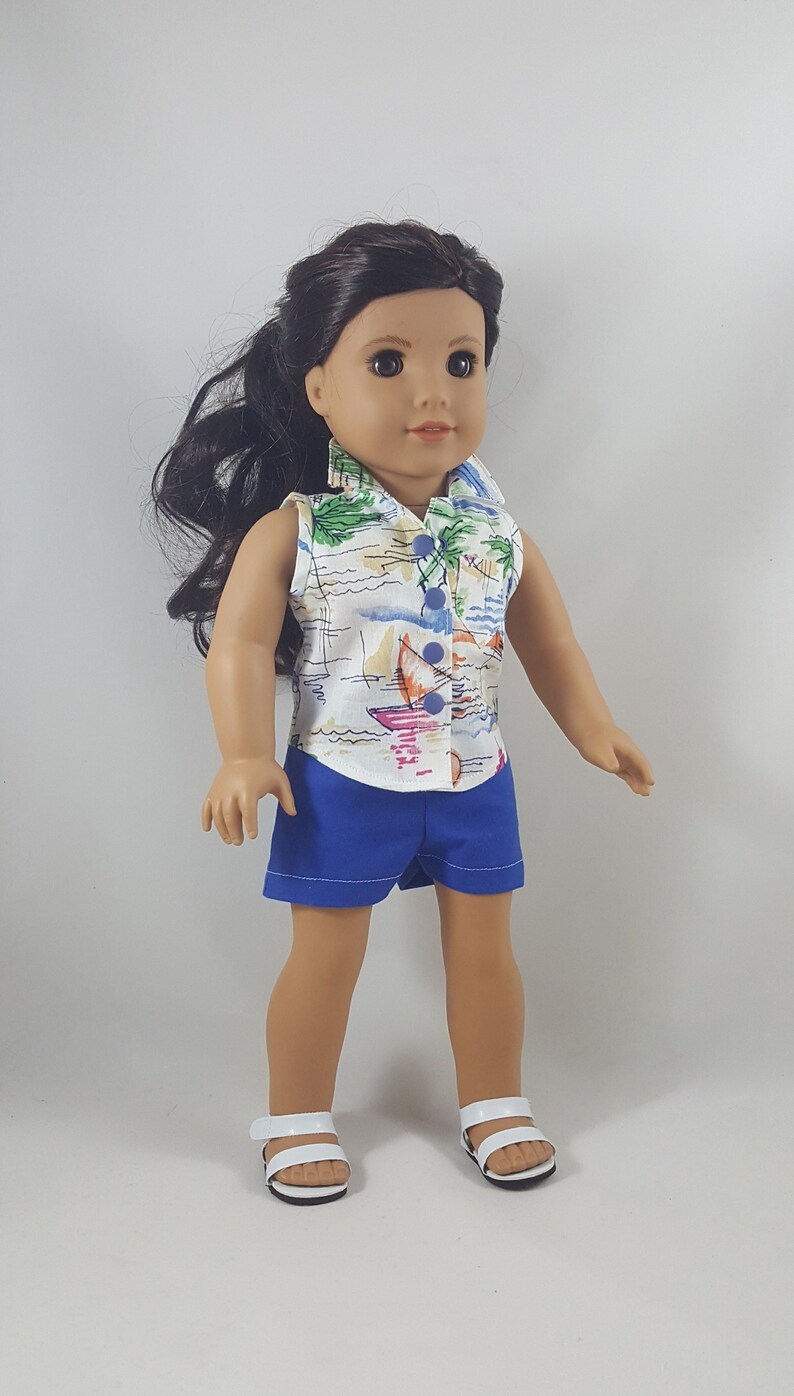 Peut inclure: Une poup&eacute;e portant une chemise blanche sans manches avec un imprim&eacute; tropical et un short en jean bleu. La poup&eacute;e a les cheveux bruns et les yeux bruns et porte des sandales blanches.