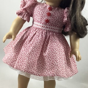 May include: A doll wearing a red and white floral dress with red buttons and a white lace petticoat. The doll has brown hair and green eyes and is wearing red shoes.