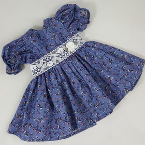 May include: A blue and white floral print dress with a white lace trim and a white flower accent. The dress has puffed sleeves and a gathered skirt.