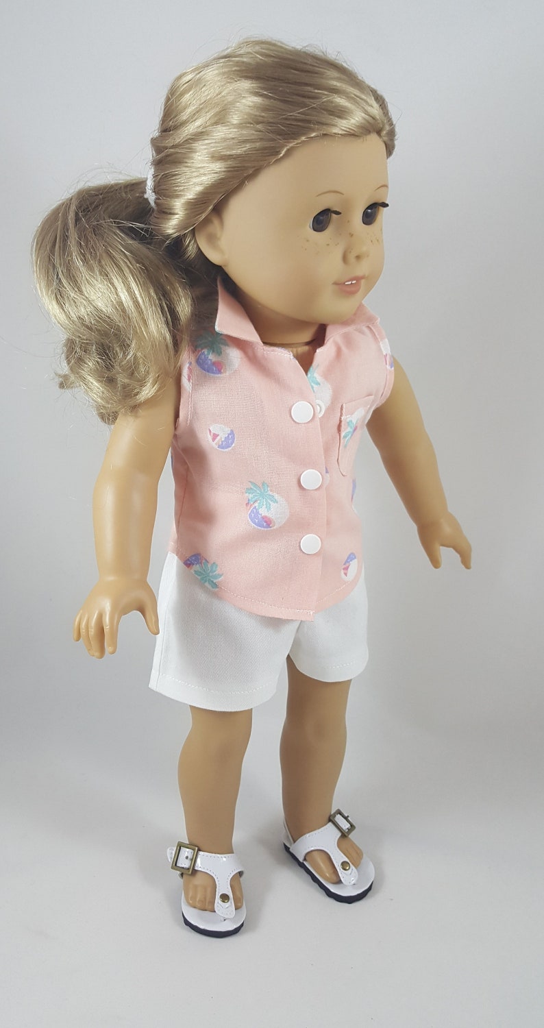Peut inclure: Une poup&eacute;e portant une chemise rose sans manches avec un imprim&eacute; tropical et un short blanc. La poup&eacute;e a les cheveux blonds et les yeux bruns. La poup&eacute;e porte des sandales blanches avec des boucles brunes.