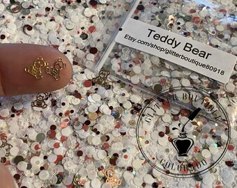 May include: A close-up of a small bag of gold glitter with a white label that reads "Teddy Bear Etsy.com/shop/glitterboutique80918". The glitter is in the shape of teddy bears.