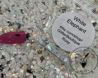 May include: White glitter with small white and black elephant shapes. The glitter is in a clear plastic bag with a white label that says "White Elephant etsy.com/shop/GlitterBoutique Roxy".